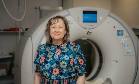 Image shows a woman in a flower print dress standing in front of an MRI machine